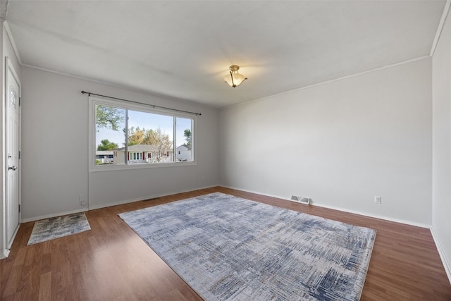empty room featuring wood finished floors, baseboards, and ornamental molding