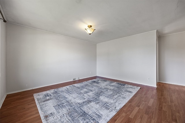 empty room featuring wood finished floors, baseboards, and crown molding