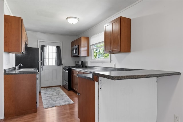 kitchen featuring appliances with stainless steel finishes, a peninsula, dark wood-style floors, dark countertops, and a breakfast bar area