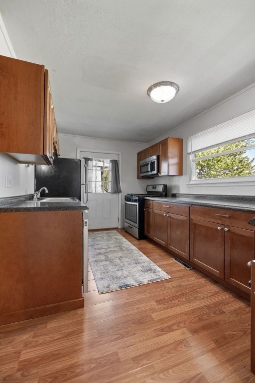 kitchen with stainless steel appliances, dark countertops, light wood finished floors, and brown cabinetry