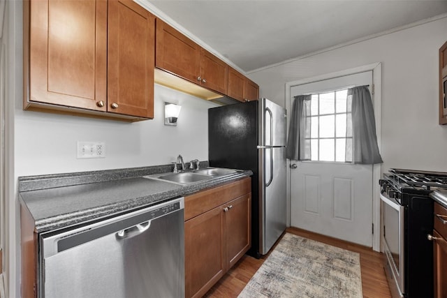 kitchen featuring appliances with stainless steel finishes, a sink, brown cabinets, dark countertops, and wood finished floors