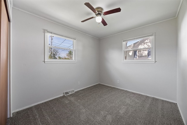 empty room featuring healthy amount of natural light, carpet floors, ornamental molding, ceiling fan, and baseboards