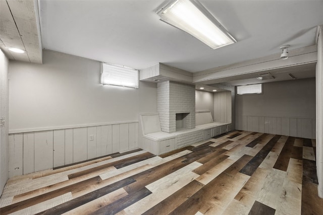 below grade area with a wainscoted wall, wood finished floors, and a brick fireplace