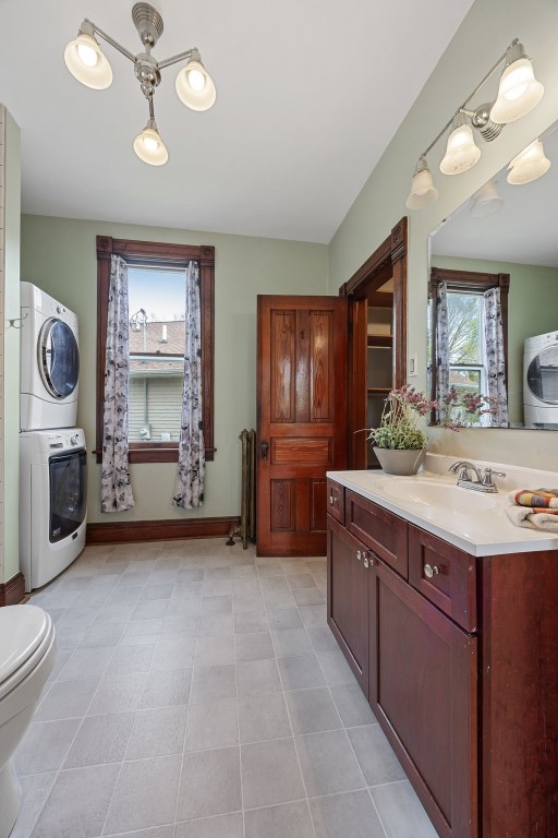 bathroom featuring stacked washing machine and dryer, toilet, vanity, and baseboards