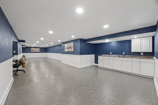 interior space featuring a wainscoted wall, a sink, a textured wall, recessed lighting, and a decorative wall