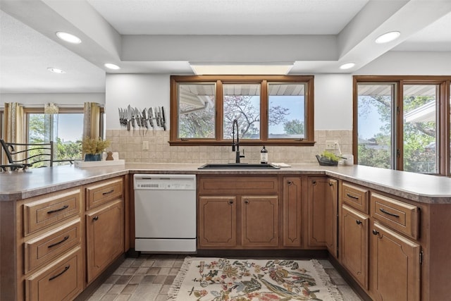 kitchen featuring white dishwasher, a peninsula, a sink, recessed lighting, and decorative backsplash