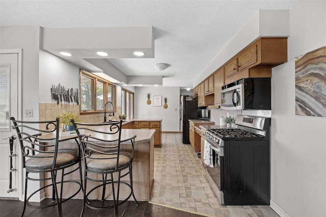 kitchen with appliances with stainless steel finishes, a peninsula, backsplash, a sink, and a textured ceiling