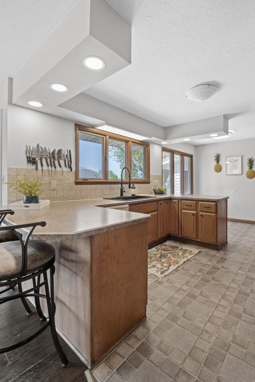 kitchen with a peninsula, a sink, tasteful backsplash, brown cabinets, and a textured ceiling