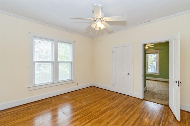 spare room with light wood-style flooring, healthy amount of natural light, crown molding, baseboards, and a ceiling fan