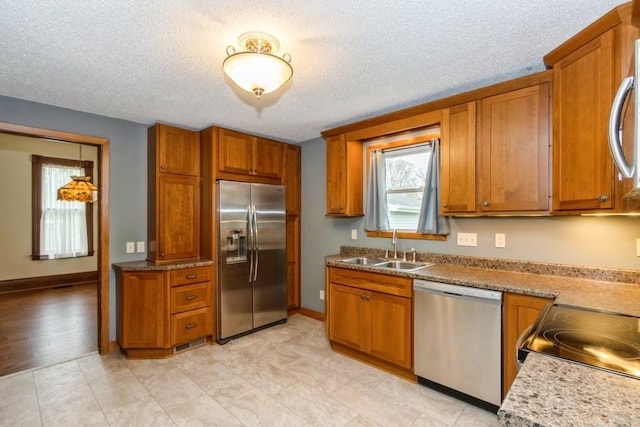 kitchen featuring appliances with stainless steel finishes, a sink, brown cabinetry, a textured ceiling, and baseboards