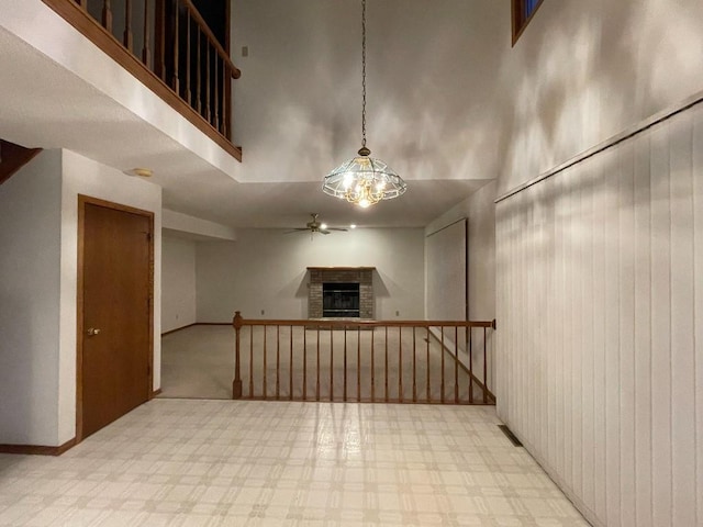 empty room with a brick fireplace, a towering ceiling, a ceiling fan, and a chandelier