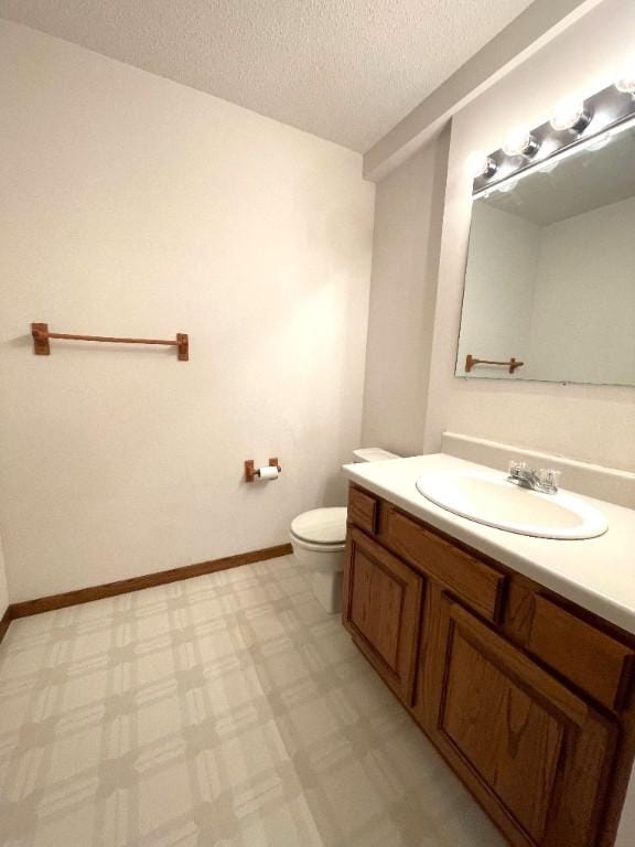 half bath with a textured ceiling, toilet, vanity, and baseboards