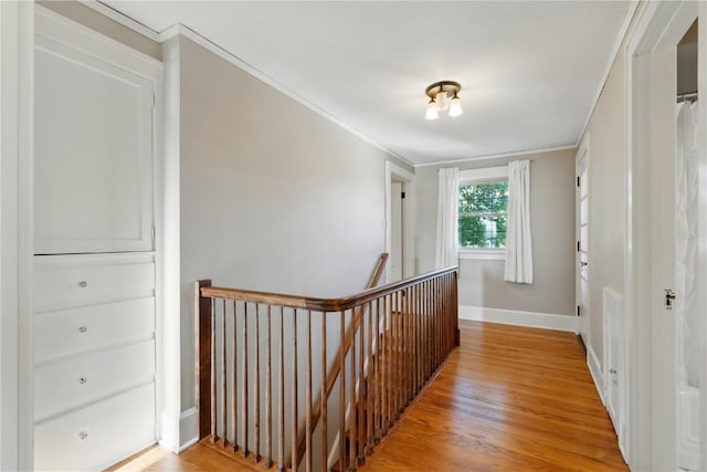 hall with an upstairs landing, ornamental molding, light wood finished floors, and baseboards