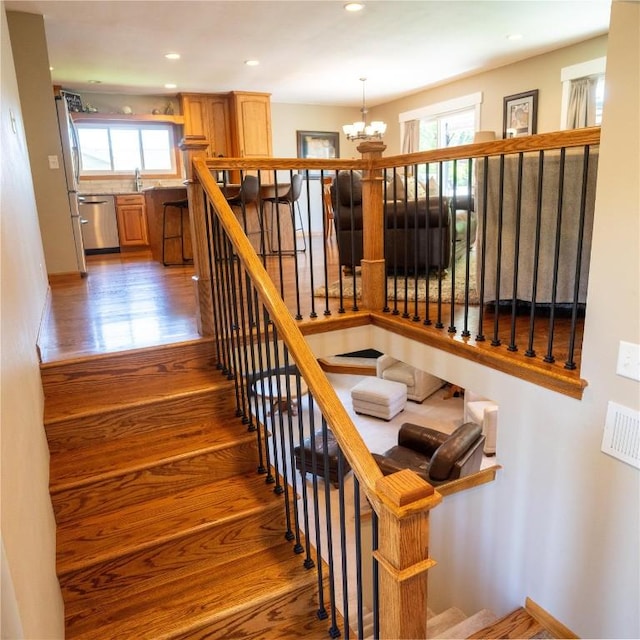 stairway with a chandelier, wood finished floors, and recessed lighting