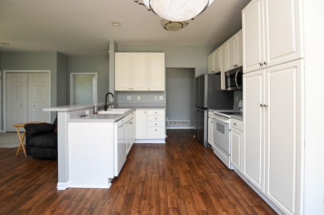 kitchen with white appliances, a sink, a peninsula, dark wood-type flooring, and white cabinetry