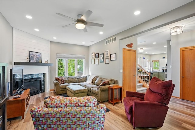 living area featuring ceiling fan, a glass covered fireplace, light wood-style floors, stairs, and recessed lighting