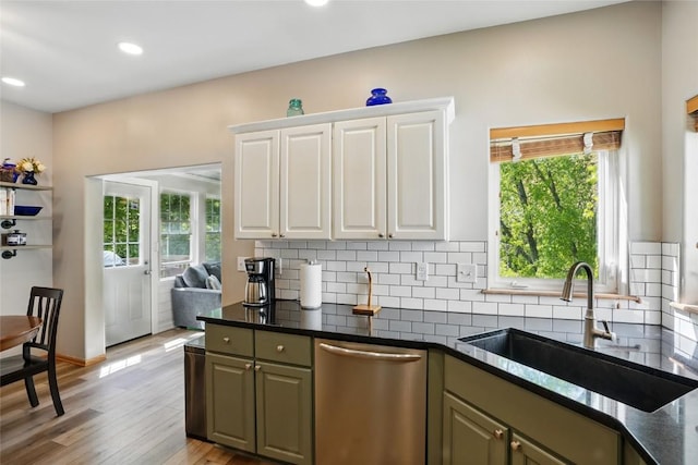 kitchen with stainless steel dishwasher, a sink, backsplash, white cabinets, and light wood-style flooring
