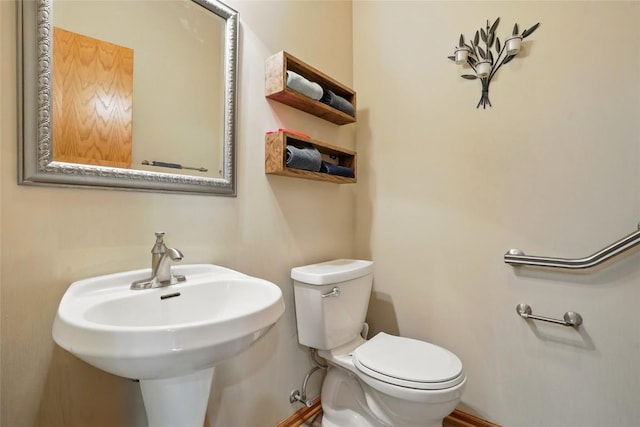 half bath featuring toilet, baseboards, and a sink