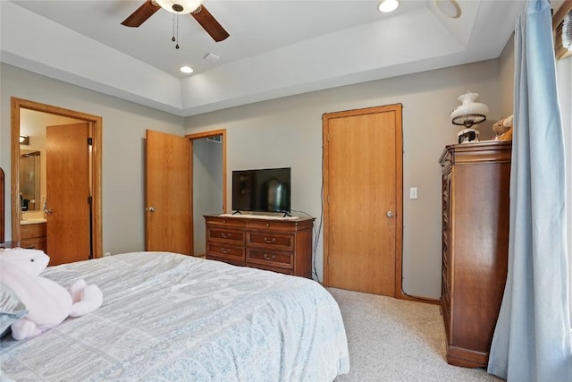 bedroom featuring a tray ceiling, light colored carpet, a ceiling fan, ensuite bathroom, and recessed lighting