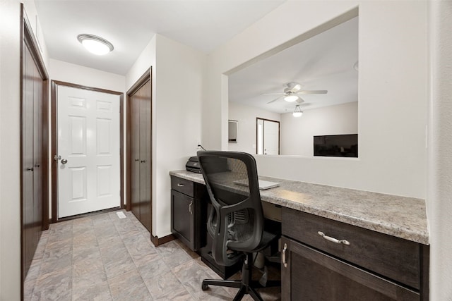 office space featuring built in desk, a ceiling fan, baseboards, and stone finish floors