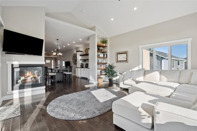 living area featuring wood finished floors, a glass covered fireplace, high vaulted ceiling, recessed lighting, and a chandelier