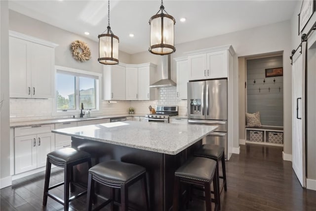 kitchen with stainless steel appliances, wall chimney range hood, a center island, a barn door, and white cabinets