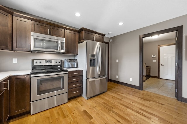 kitchen featuring appliances with stainless steel finishes, dark brown cabinets, light countertops, light wood-style floors, and recessed lighting