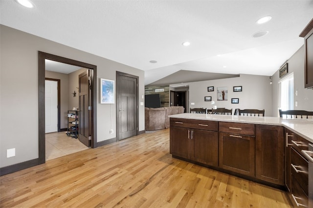kitchen featuring light wood-style flooring, light countertops, dark brown cabinets, open floor plan, and baseboards