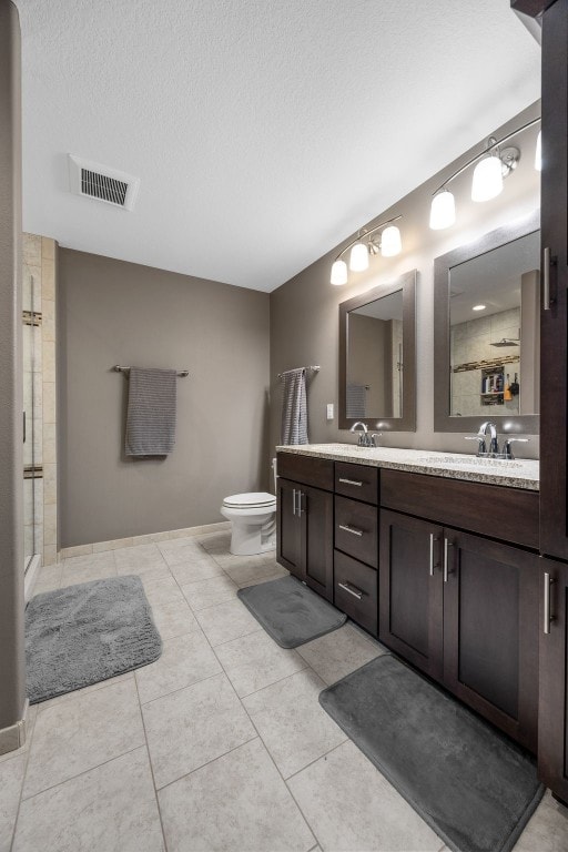 bathroom featuring a textured ceiling, toilet, double vanity, a shower with door, and tile patterned floors