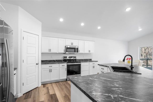kitchen featuring stainless steel appliances, a sink, light wood finished floors, white cabinets, and vaulted ceiling