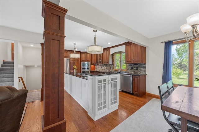 kitchen with stainless steel appliances, dark countertops, wood finished floors, backsplash, and plenty of natural light