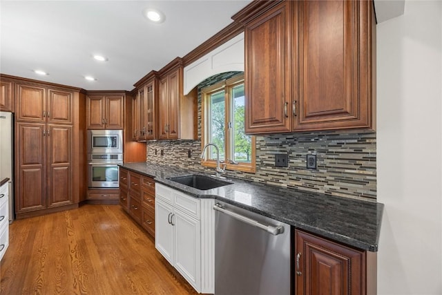 kitchen featuring appliances with stainless steel finishes, a sink, recessed lighting, wood finished floors, and glass insert cabinets