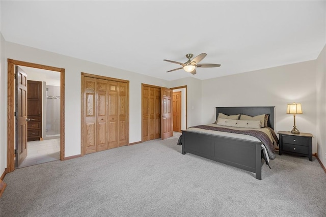 bedroom featuring light colored carpet, two closets, baseboards, ensuite bath, and ceiling fan