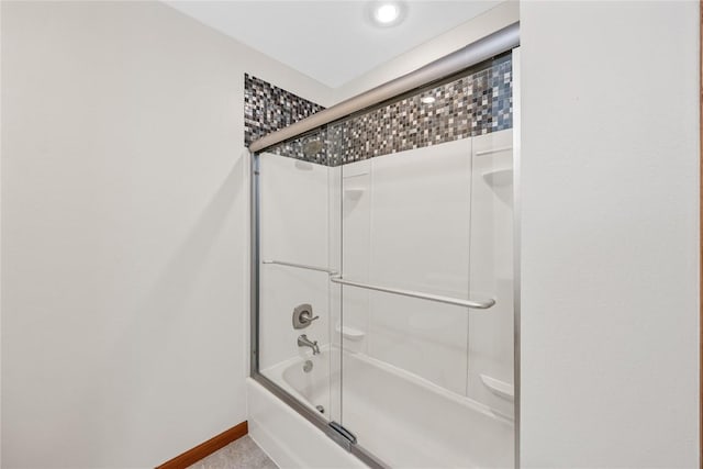 bathroom featuring bath / shower combo with glass door and baseboards