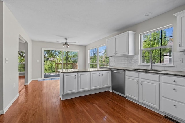 kitchen with dishwasher, a sink, a peninsula, decorative backsplash, and white cabinets