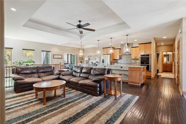 living room with a tray ceiling, a ceiling fan, recessed lighting, and dark wood finished floors