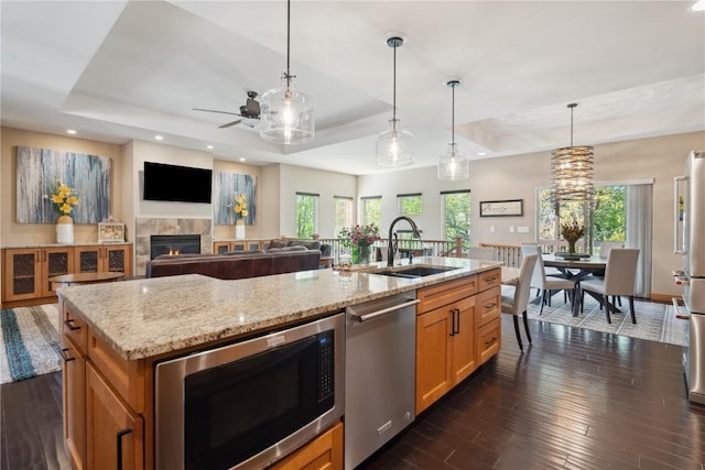 kitchen with stainless steel appliances, a raised ceiling, a ceiling fan, a sink, and a tiled fireplace