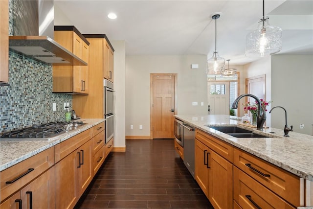 kitchen with appliances with stainless steel finishes, wall chimney range hood, a sink, tasteful backsplash, and light stone counters