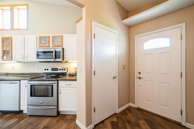 kitchen with appliances with stainless steel finishes, white cabinetry, dark countertops, dark wood finished floors, and glass insert cabinets