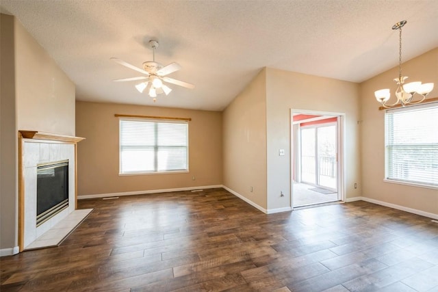 unfurnished living room with a chandelier, a ceiling fan, dark wood-style floors, a tiled fireplace, and baseboards