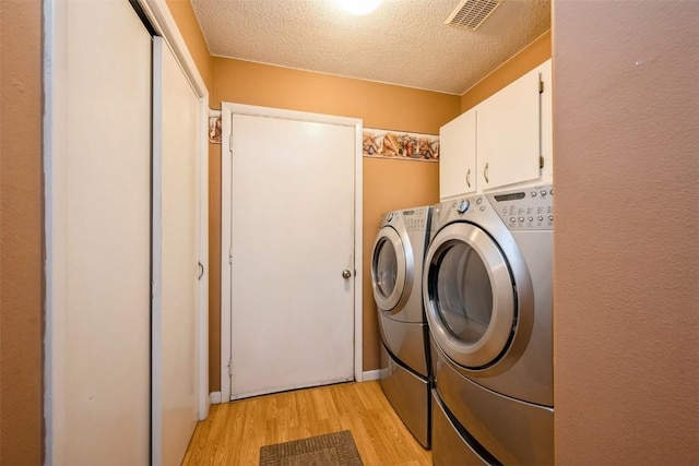 laundry room featuring separate washer and dryer, light wood finished floors, cabinet space, and a textured ceiling