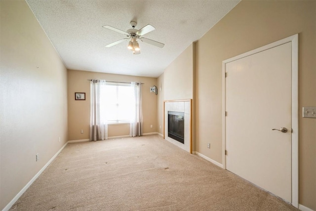 unfurnished living room with ceiling fan, a fireplace, a textured ceiling, light colored carpet, and baseboards