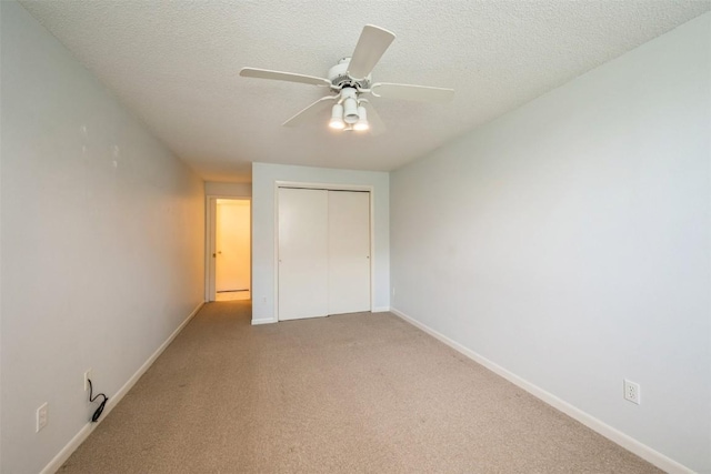 unfurnished bedroom featuring a closet, light carpet, baseboards, ceiling fan, and a textured ceiling