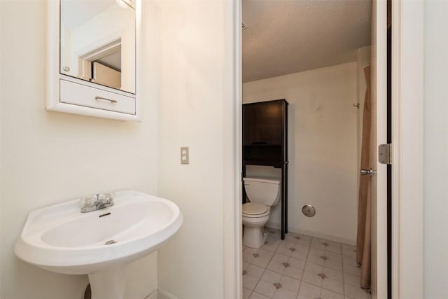bathroom with toilet, a sink, tile patterned floors, a textured ceiling, and baseboards