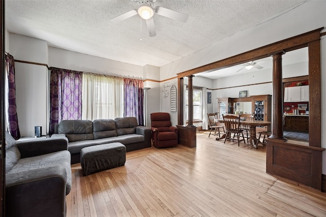 living room featuring a ceiling fan, a textured ceiling, decorative columns, and light wood-style floors
