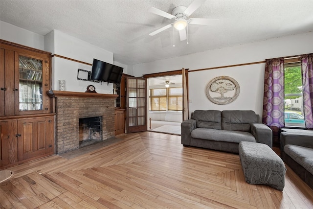 living room with a ceiling fan, a brick fireplace, a textured ceiling, and parquet floors