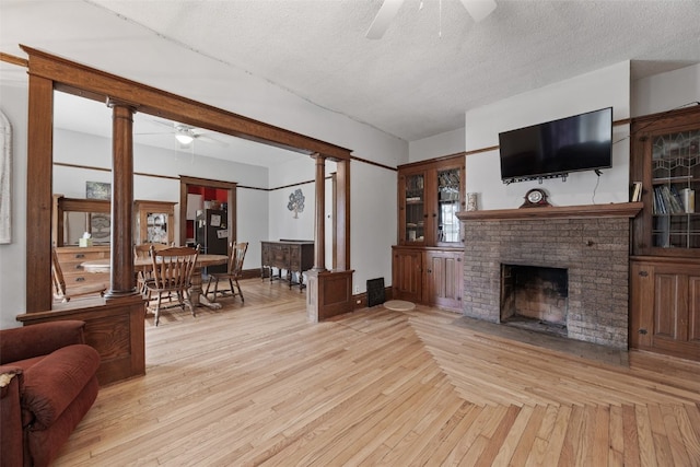 living room featuring ceiling fan, ornate columns, a fireplace, a textured ceiling, and baseboards
