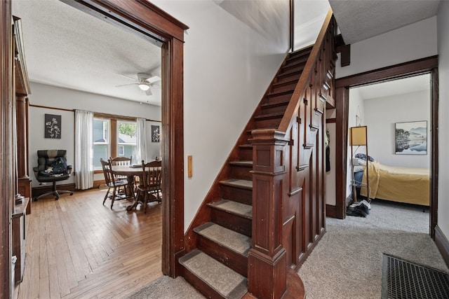 staircase with a ceiling fan, a textured ceiling, and wood finished floors