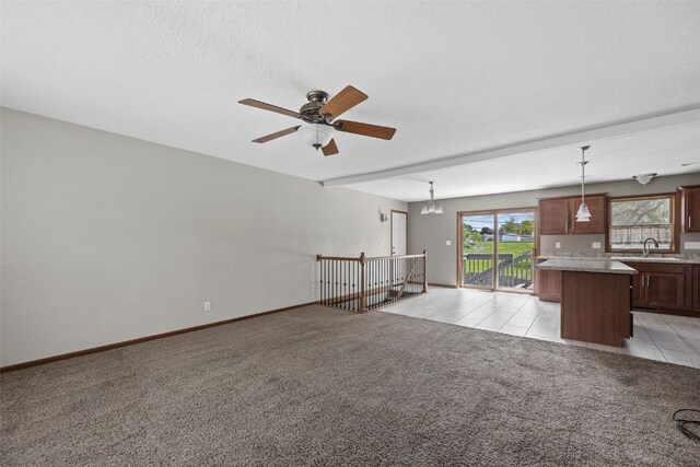 unfurnished living room featuring a sink, light carpet, a ceiling fan, and baseboards