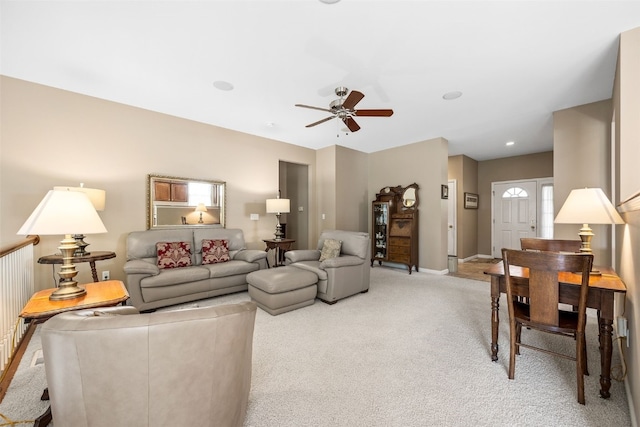 living area featuring light colored carpet, ceiling fan, and baseboards
